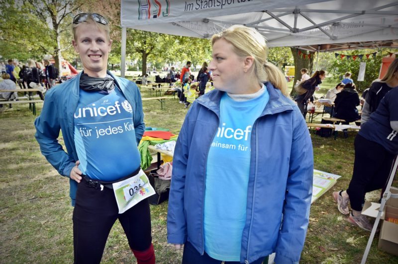 Zwei Menschen mit blauer Kleidung von UNICEF stehen auf einer Wiese.