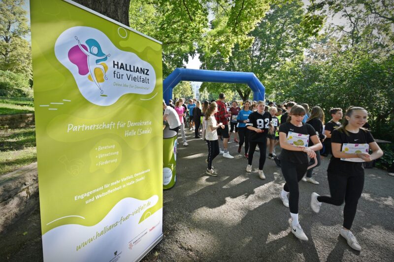 Eine Gruppe Personen läuft durch eine Start. und Ziel-Linie. Links steht ein Banner mit dem HALLIANZ Logo.
