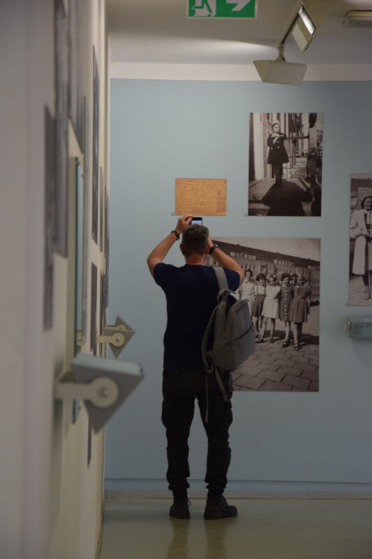 Eine Person steht in einer Ausstellung und fotografiert ein ausgestelltes Dokument..