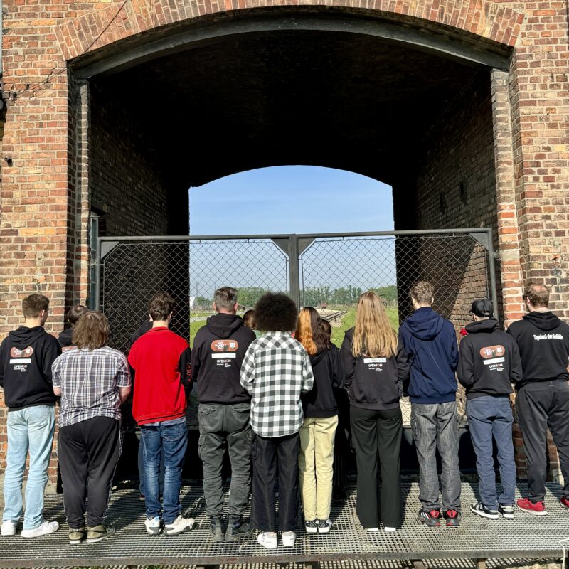 Junge Personen stehen an dem Tor einer Gedenkstätte.