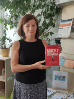 Eine Person schaut in die Kamera und hält das Buch "Machtübernahme: Was passiert, wenn Rechtsextremisten regieren - Eine Anleitung zum Widerstand" in der Hand.