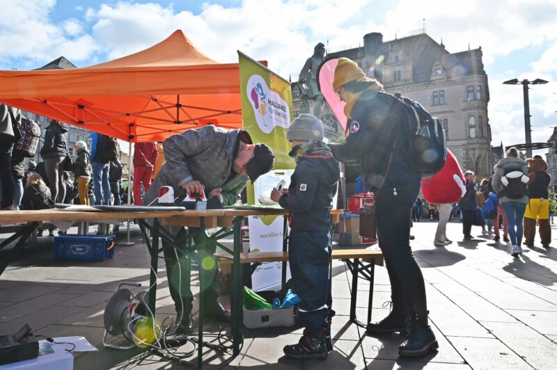 Drei Perosnen stehen an einem Stand, einer von ihnen edruckt einen Beutel.