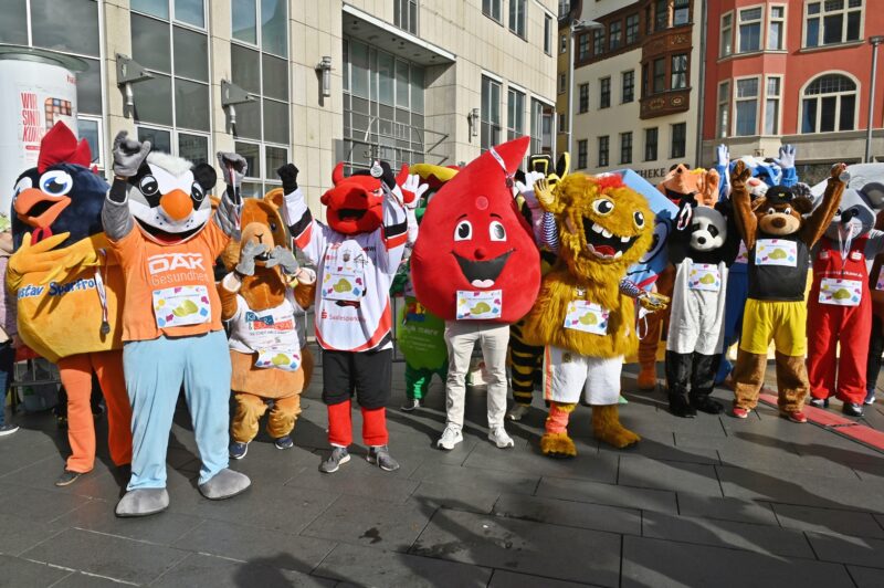 Eine Gruppe Maskottchen steht mit Medallien zusammen und winkt in die Kamera.