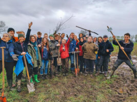 Eine Gruppe junger Personen steht mit Schaufeln auf einem Acker und lächelt in die Kamera.