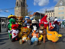 14 Maskottchen von Unternehmen und Vereinen stehen auf dem Markt der Stadt Halle vor dem Roten Turm für ein Gruppenbild zusammen.